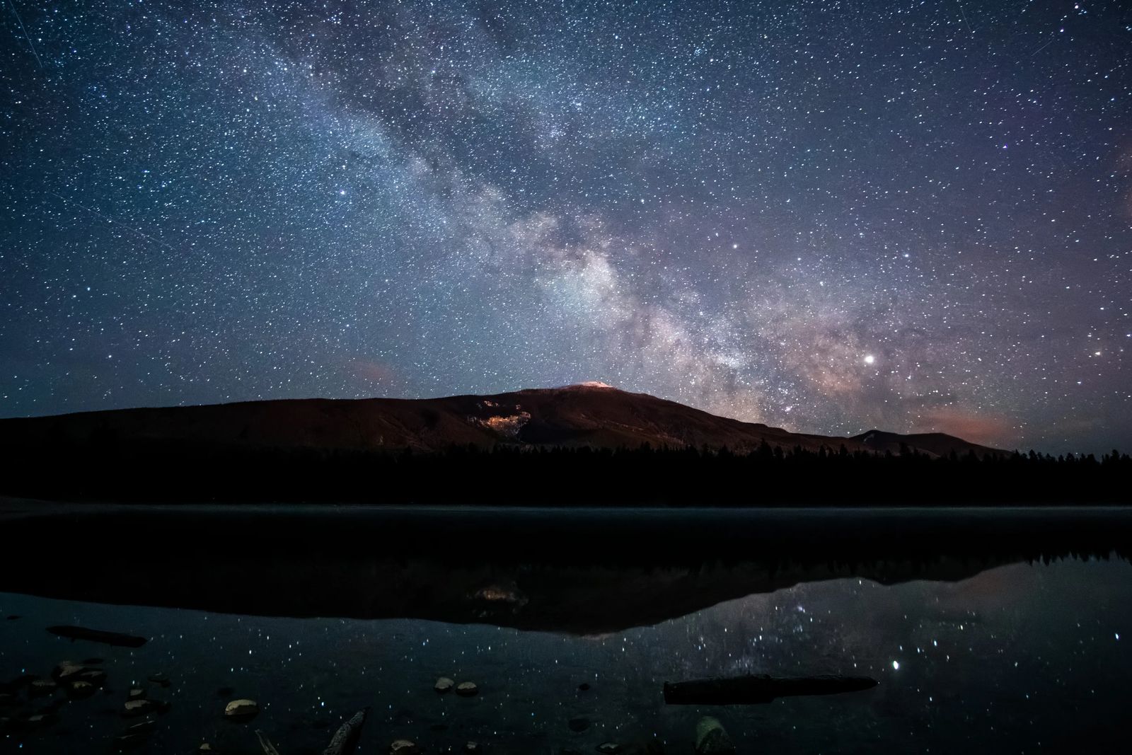 Jasper Dark Sky with Galaxy above and reflecting in the lake below with a silhouette of a mountain between- Best places to visit in Jasper National Park