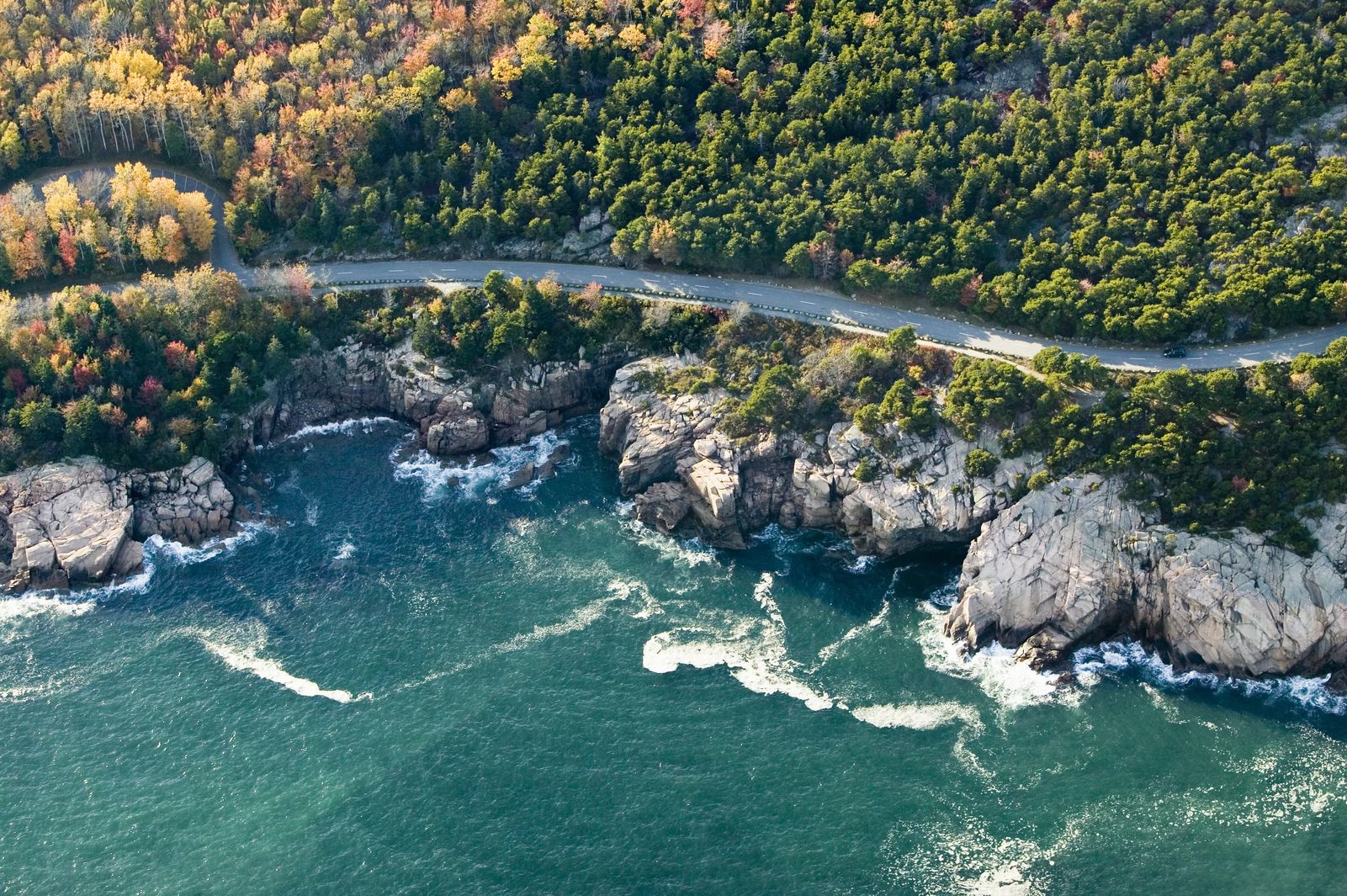 drone shot from above with a winding road through forest right next to the coast of Maine