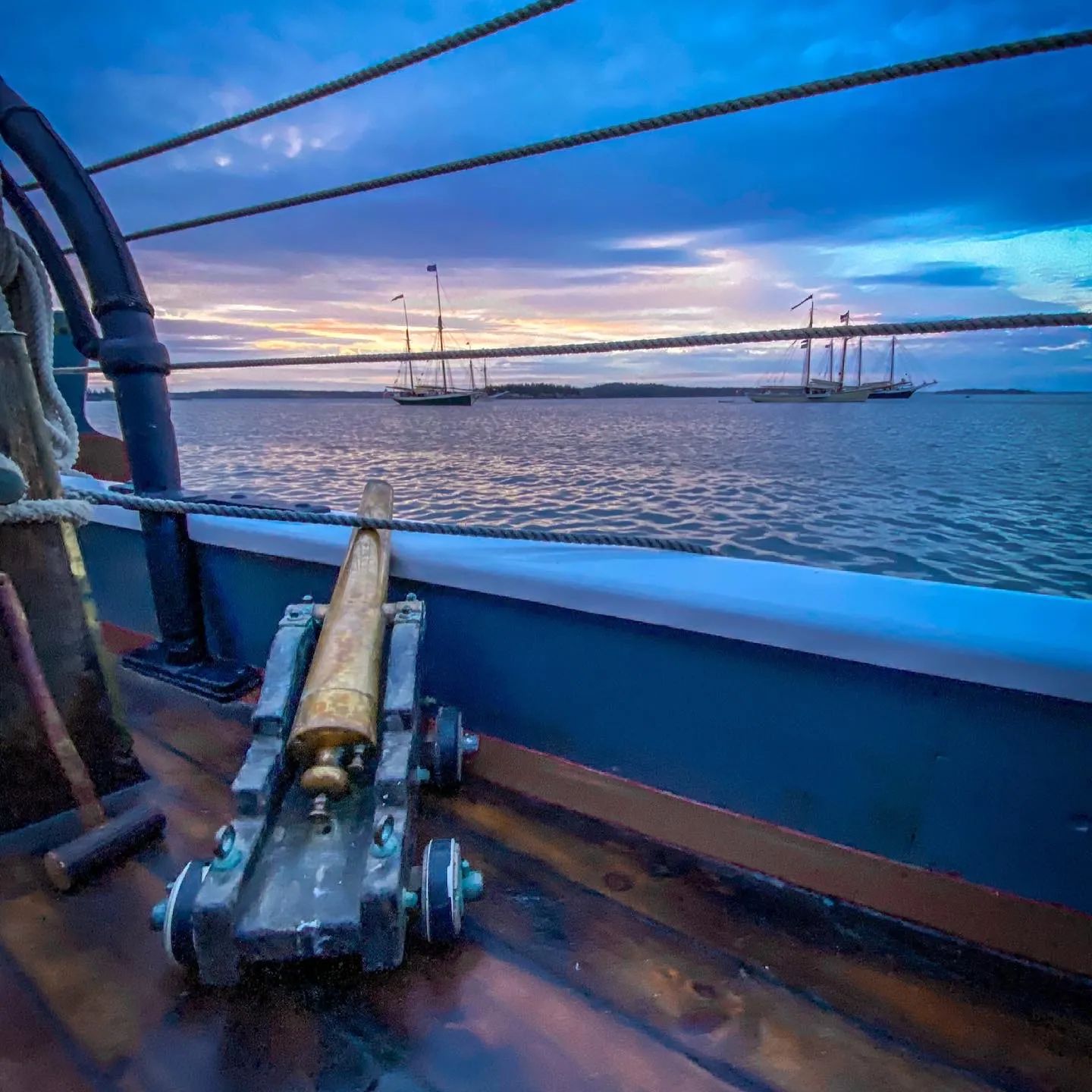 Sailing the Islands of Maine, a small cannon against the sunset and ships in the background