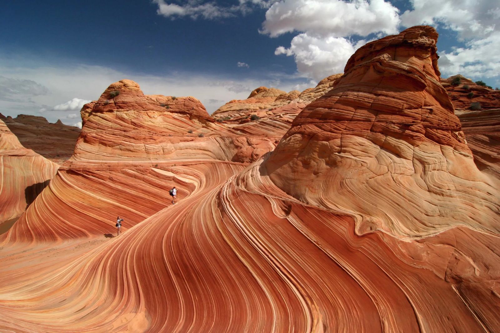 two hikers on the lines of the wave, with mountains towering above