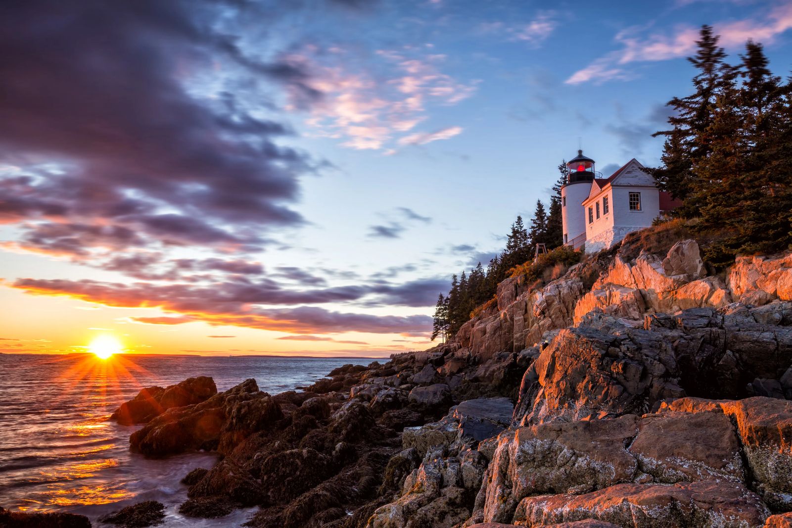 pink sunset with a sunburst against rocky cliffs on the coast of Maine